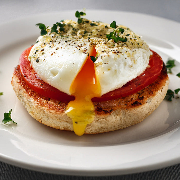 Toasted english muffin, topped with an overeasy egg and a slice of tomato, with herb mayonnaise on top on a white plate