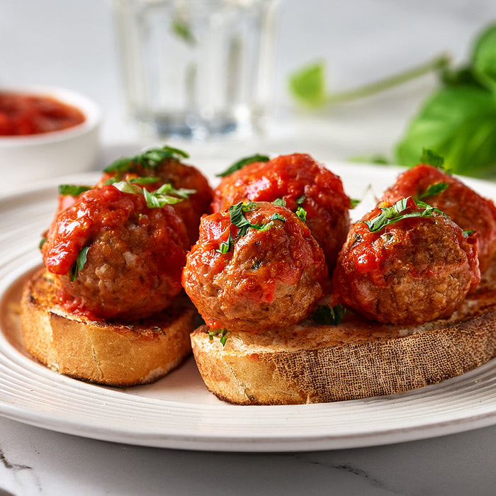 Italian meatballs topped with tomato sauce on toasted bread on a white plate on a white marble countertop