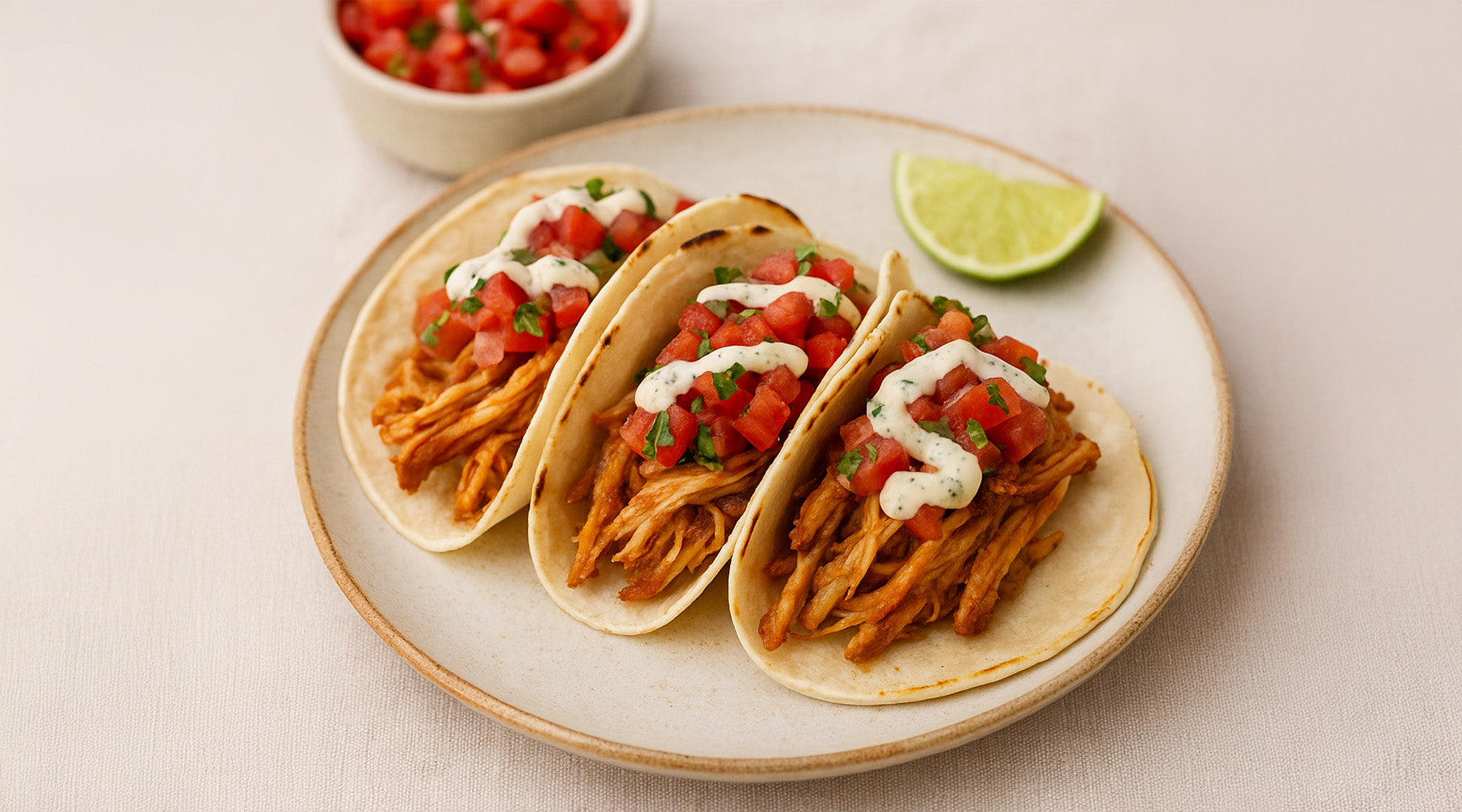 Slow Cooker Tequila Chicken Tacos with a Creamy Jalapeno Sauce on a plate with a lime wedge on the side