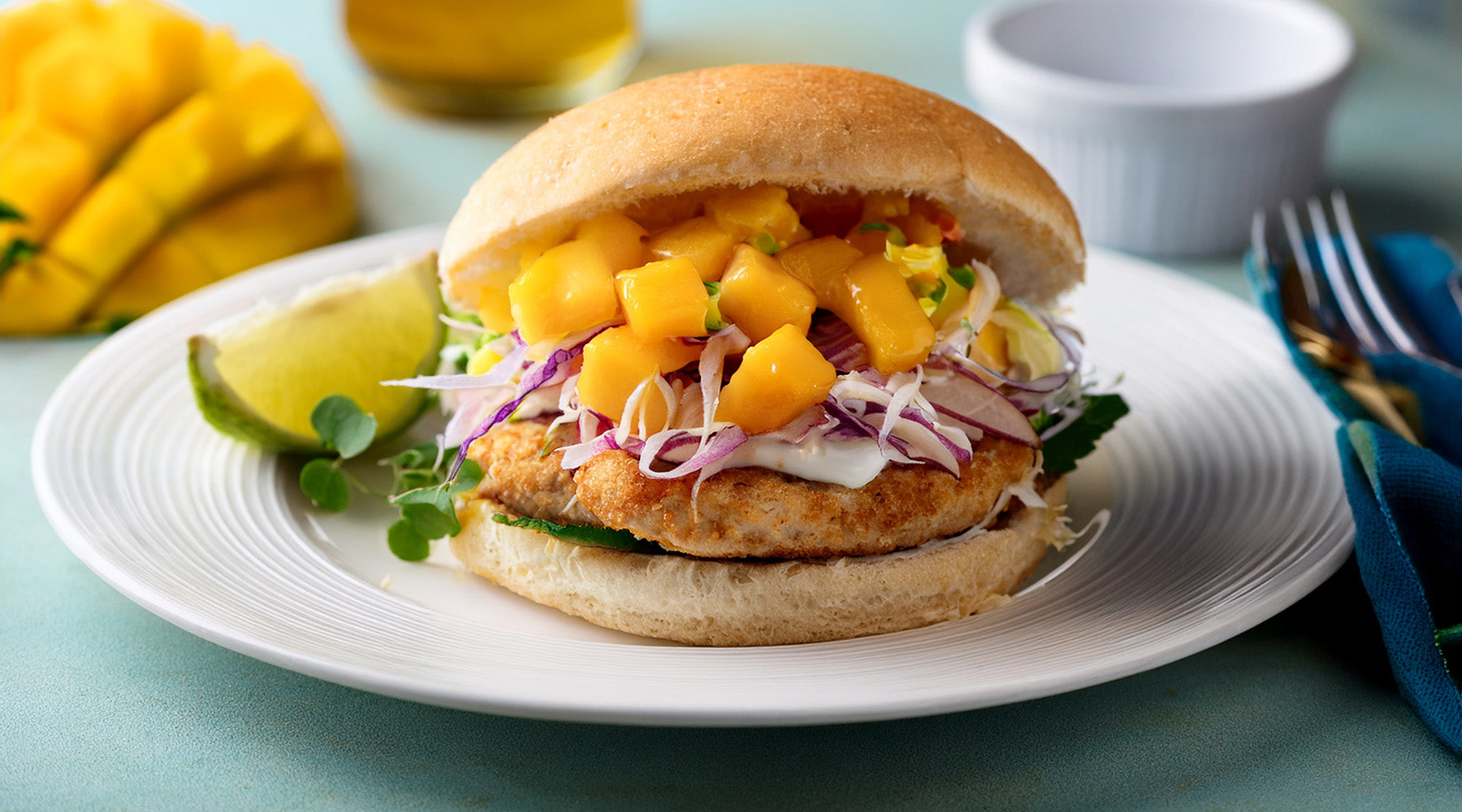 Turkey burger on a toasted bun topped with mango slaw on a white plate